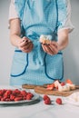 cropped shot of woman in apron spreading cream cheese on baguette over table with strawberries and raspberries